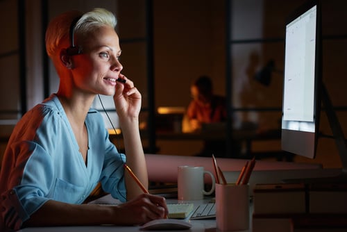 ヘッドホンを着けてパソコン作業をしている若い女性 Young woman in headphones working on computer while sitting at her workplace